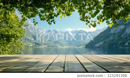 A serene vista of mountains and lake, framed by lush foliage and a wooden deck, invites contemplation and escape into nature's embrace. A serene vista of mountains and lake, framed by lush foliage and a wooden deck, invites contemplation and escape into nature's embrace. 123291306
