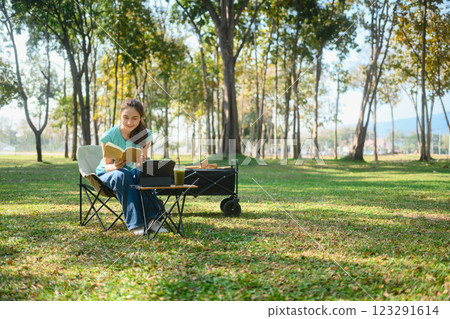Cheerful woman sitting on foldable chair in a green park, reading a book 123291614