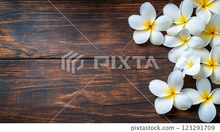 Wooden backdrop adorned with tropical flowers featuring white petals and bright yellow centers, creating a serene and natural composition. 123291709