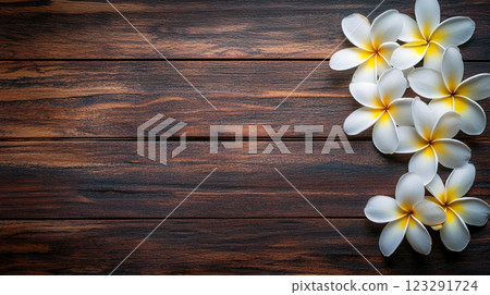 A rustic wood background with a string of delicate white and yellow tropical flowers, embodying nature's simple beauty. 123291724