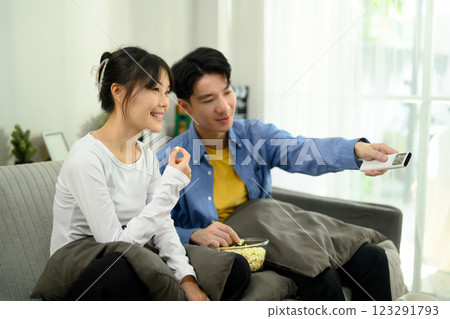 Happy young couple watching TV at home and sharing a bowl of popcorn 123291793