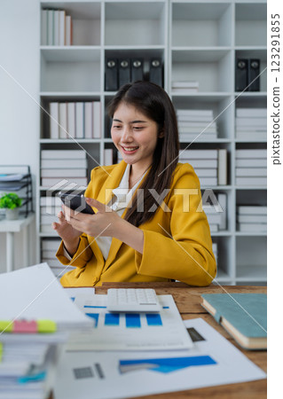 young businesswoman in a bright yellow suit smiling while using smartphone in a modern office environment young businesswoman in a bright yellow suit smiling while using smartphone in a modern office environment 123291855