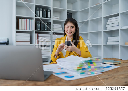young businesswoman in a bright yellow suit smiling while using smartphone in a modern office environment young businesswoman in a bright yellow suit smiling while using smartphone in a modern office environment 123291857