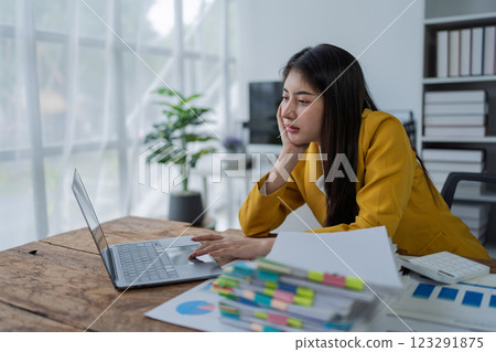 Young asian businesswoman working focusedly on laptop surrounded by documents and charts in bright modern office Young asian businesswoman working focusedly on laptop surrounded by documents and charts in bright modern office 123291875