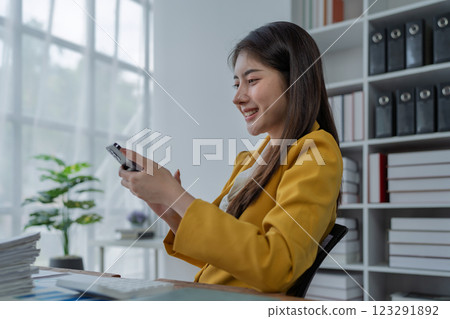Young professional woman smiling while using smartphone in modern office environment with natural light Young professional woman smiling while using smartphone in modern office environment with natural light 123291892