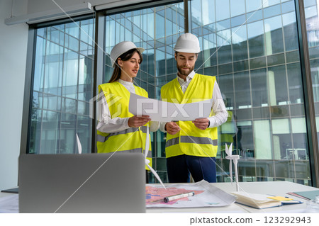 Two people in yellow vests and hard caps working together in the office 123292943