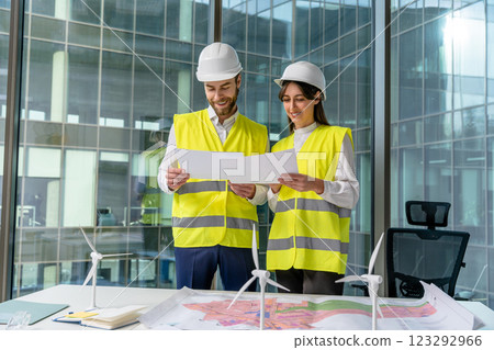 Two young engineers in yellow vests discussing new sustainability project 123292966