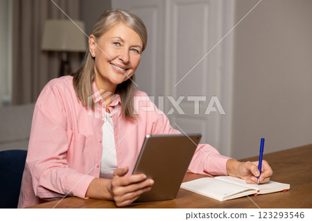 Mid aged caucasian woman sitting at the table and making notes while working 123293546