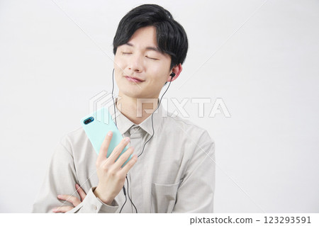一位 20 多歲的男子戴著耳機在白色背景上聽音樂 123293591