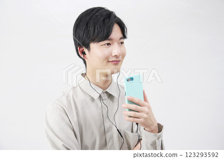 A man in his 20s listening to music with earphones on a white background 123293592
