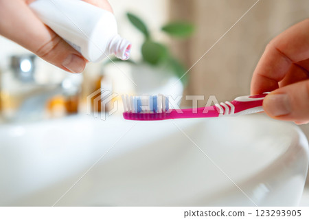 Morning routine close-up of a woman's hand squeezing toothpaste onto a toothbrush. She brushes her teeth, ensuring hygiene and fresh breath. Morning routine close-up of a woman's hand squeezing toothpaste onto a toothbrush. She brushes her teeth, ensuring hygiene and fresh breath. 123293905