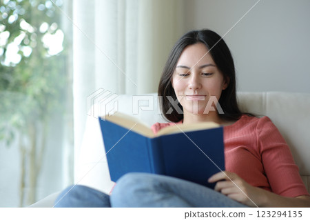Satisfied asian woman reading a paper book at home Satisfied asian woman reading a paper book at home 123294135