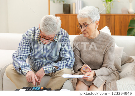 Middle aged senior couple sit with laptop and paper document. Older mature man woman reading paper bill pay online at home managing bank finances calculating taxes planning loan debt pension payment Middle aged senior couple sit with laptop and paper document. Older mature man woman reading paper bill pay online at home managing bank finances calculating taxes planning loan debt pension payment 123294949