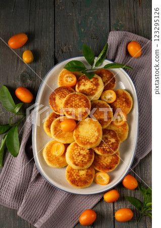 Delicious cheesecakes with delicious kumquats in a large oval plate, top view Delicious cheesecakes with delicious kumquats in a large oval plate, top view 123295126