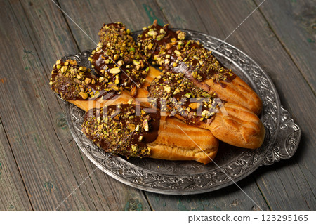 Chocolate and pistachio eclair on a vintage metal plate Chocolate and pistachio eclair on a vintage metal plate 123295165
