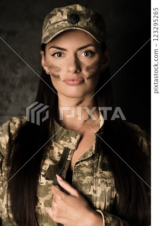 Portrait of a young woman in a military uniform and a cap with the coat of arms of Ukraine. The woman has camouflage on her face 123295265