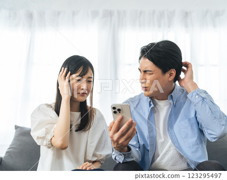 一對夫婦在客廳看著他們的智慧型手機,憂心忡忡 一對夫婦在客廳看著他們的智慧型手機,憂心忡忡 123295497