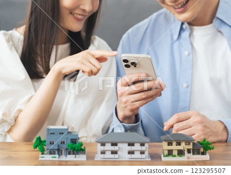 Couple looking at smartphone in front of house model, room search, real estate investment 123295507