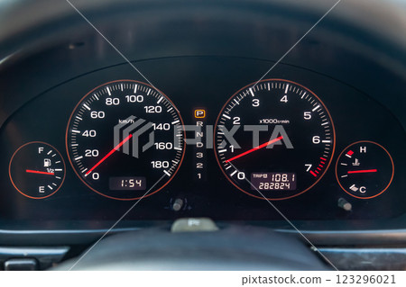 Car dashboard with red instrument circles with backlit arrows at night with a speedometer, tachometer with a mechanical gearshift gearbox to monitor the condition of the car on a black background. Car dashboard with red instrument circles with backlit arrows at night with a speedometer, tachometer with a mechanical gearshift gearbox to monitor the condition of the car on a black background. 123296021