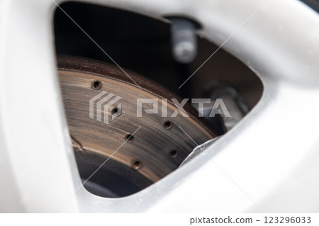 Close-up on a part of an aluminum wheel through the spokes of which a perforated brake disc of a sports car are visible. Auto service industry. Close-up on a part of an aluminum wheel through the spokes of which a perforated brake disc of a sports car are visible. Auto service industry. 123296033