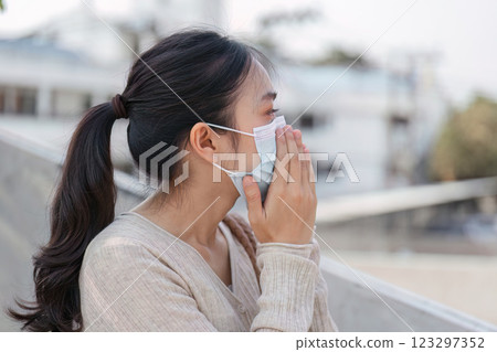 Young woman wearing a mask outdoors, expressing concern about pollution and air quality. 123297352