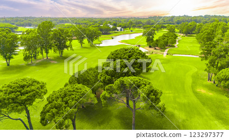 Panoramic view of a golf course with a winding river, lush greenery, and a vibrant sunset sky Panoramic view of a golf course with a winding river, lush greenery, and a vibrant sunset sky 123297377
