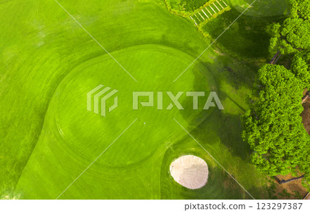 Aerial view of a golf course with a sand trap and manicured green surrounded by lush trees 123297387