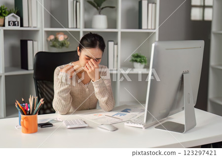 Stressed office worker rubbing her forehead in frustration while working on a computer. 123297421