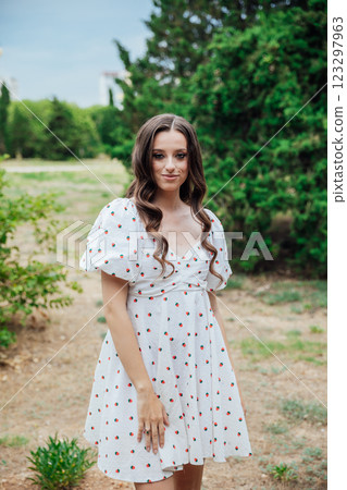Beautiful brunette woman in summer dress walking in the park Beautiful brunette woman in summer dress walking in the park 123297963