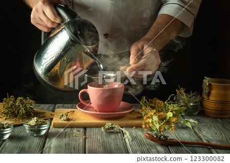 Steam rises as a skilled hand pours hot water over carefully selected herbs into a pink cup. The kitchen is filled with the earthy aroma of nature's remedies, creating a cozy atmosphere 123300082