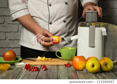 Experienced chef in white uniform adding sliced apples to electric juicer. Making delicious and healthy apple juice in restaurant or hotel kitchen for dinner. Apple diet Experienced chef in white uniform adding sliced apples to electric juicer. Making delicious and healthy apple juice in restaurant or hotel kitchen for dinner. Apple diet 123300087