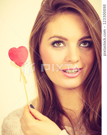 Flirty woman holding red wooden heart on stick 123300898