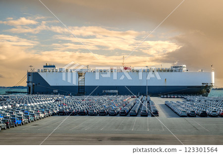 Large vehicle or car carrier ship known as RO-RO, roll on roll off, at port on sunny day, large parking area filled with cars. Blue sky and colorful clouds, vehicle transportation. Large vehicle or car carrier ship known as RO-RO, roll on roll off, at port on sunny day, large parking area filled with cars. Blue sky and colorful clouds, vehicle transportation. 123301564