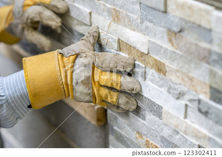 Closeup of manual worker in protection gloves pushing the tile into the cement on the wall Closeup of manual worker in protection gloves pushing the tile into the cement on the wall 123302411