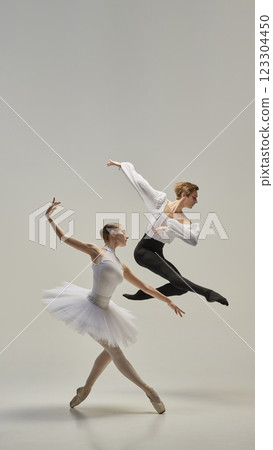 Ballet dancers performing synchronized leap, arms and legs fully extended in fluid, weightless motion against white studio background. 123304450