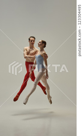 Dynamic photo of young ballet duo, athletic man and woman, leaping in motion gracefully in synchronized motion against white studio background. Dynamic photo of young ballet duo, athletic man and woman, leaping in motion gracefully in synchronized motion against white studio background. 123304495