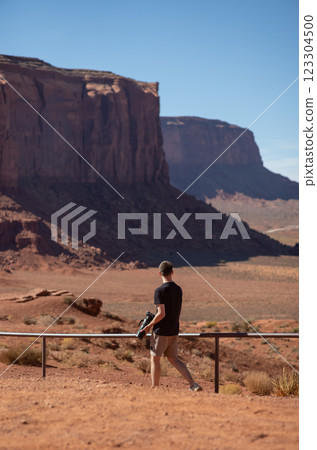Photographer exploring the vast landscape of Monument Valley. Young man with camera walking in Monument Valley area. Concept of adventure, travel, creativity, and solitude in nature. Photographer exploring the vast landscape of Monument Valley. Young man with camera walking in Monument Valley area. Concept of adventure, travel, creativity, and solitude in nature. 123304500