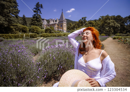 A woman wearing a white shirt and hat is sitting in a field of purple flowers A woman wearing a white shirt and hat is sitting in a field of purple flowers 123304534