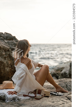 Woman Beach Relaxation - A woman in a white bikini and sunglasses sits on the beach with her legs crossed, looking out at the ocean. Woman Beach Relaxation - A woman in a white bikini and sunglasses sits on the beach with her legs crossed, looking out at the ocean. 123304573