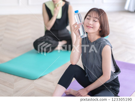 坐在瑜珈墊上拿著塑膠瓶的年輕女子 坐在瑜珈墊上拿著塑膠瓶的年輕女子 123305190