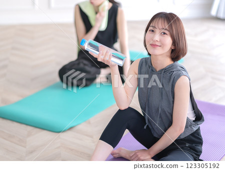 Young woman sitting on yoga mat and holding plastic bottle Young woman sitting on yoga mat and holding plastic bottle 123305192