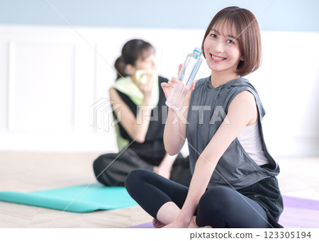 坐在瑜珈墊上拿著塑膠瓶的年輕女子 123305194