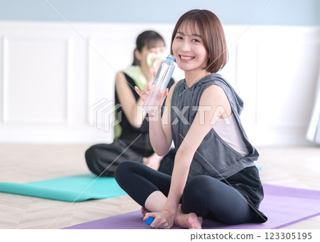 坐在瑜珈墊上拿著塑膠瓶的年輕女子 123305195