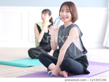 Young woman sitting on yoga mat and holding plastic bottle 123305196