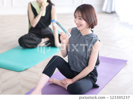 坐在瑜珈墊上拿著塑膠瓶的年輕女子 123305237