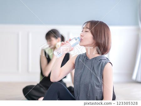 年輕女子坐在瑜珈墊上喝瓶裝水 年輕女子坐在瑜珈墊上喝瓶裝水 123305328
