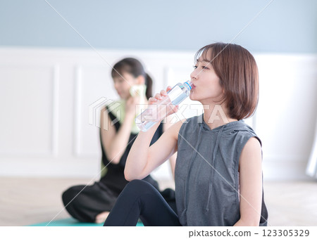 Young woman sitting on a yoga mat and drinking bottled water 123305329