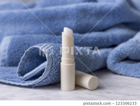 Opened white lip balm stick with a blank lid near blue bath towel top view, cosmetic mockup Opened white lip balm stick with a blank lid near blue bath towel top view, cosmetic mockup 123306233