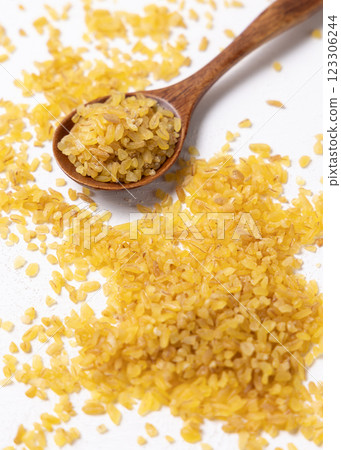 Raw dry uncooked yellow bulgur grain in a wooden spoon on white table cloesup. Ancient food 123306244