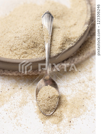 Raw uncooked fonio seeds on a plate with a metal spoon on white table. African ancient pseudocereal 123306246